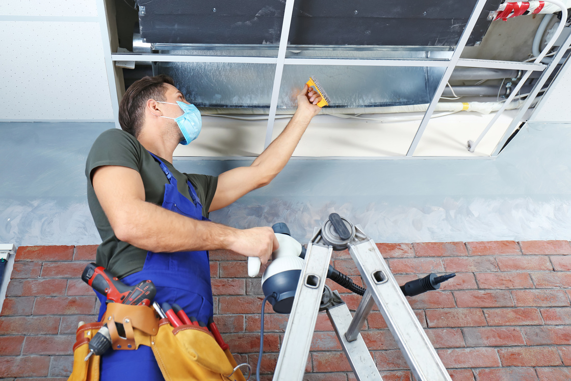 Male Technician Cleaning Industrial Air Conditioner Indoors